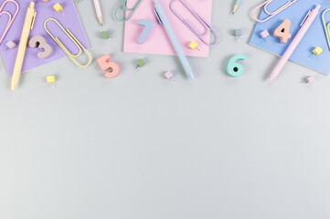 Top view of pink, purple and blue notebooks on grey background. Colorful pens, pencils, paperclips, numbers, shapes and pins. School, office wallpaper. Flat lay, copy space.