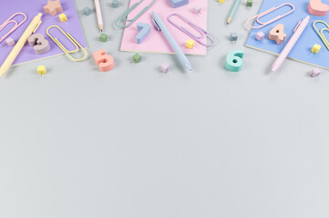 Top view of pink, purple and blue notebooks on grey background. Colorful pens, pencils, paperclips, numbers, shapes and pins. School, office wallpaper. Flat lay, copy space.