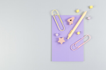 Top view of purple notebook on grey background. Paperclips, pen, number, shape and pins. School, office wallpaper. Flat lay, copy space.