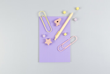 Top view of purple notebook on grey background. Paperclips, pen, number, shape and pins. School, office wallpaper. Flat lay, copy space.
