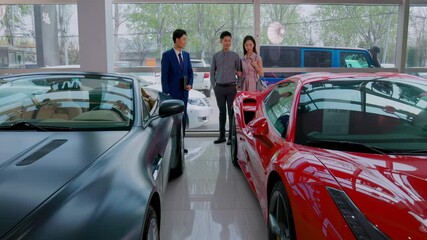 Couple with attractive auto dealer in a suit presenting new car model to his client. Buyer observing automobile thinking about purchasing. Concept of buying and selling car, car rental service. - Powered by Adobe