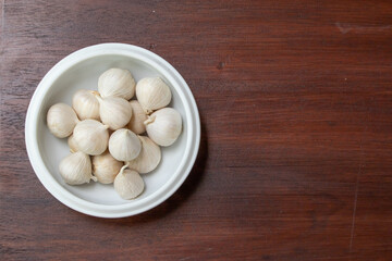 Single clover garlic or pearl garlic in ceramic bowl on wooden kitchen table, top view