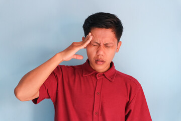 Asian young man wearing a red shirt showing pain expression while touching head with his hand