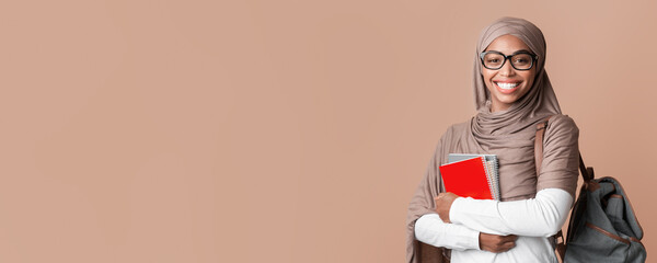 Education Concept. Portrait Of Smiling Black Muslim Girl In Hijab With Backpack And Notepads Posing Over Yellow Background With Empty Space