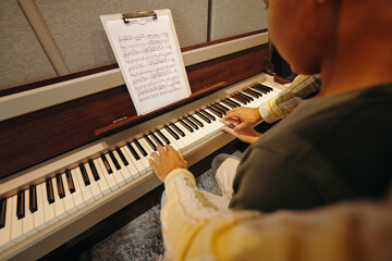 Man studying piano by following sheet music placed on clipboard, fingers pressing keys yearnly,...