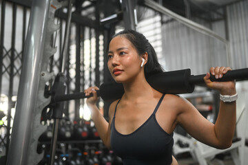 Fototapeta premium Focused sporty woman doing squat exercise with a barbell in a gym