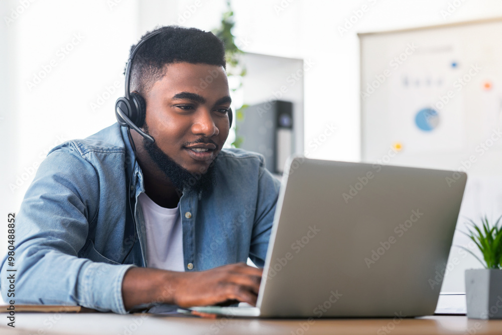 Aufkleber call center operator at work. handsome black manager wearing headset and typing at laptop, working i