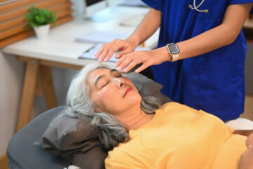 Elderly woman having Reiki healing treatment with therapist in clinic. Alternative medicine concept