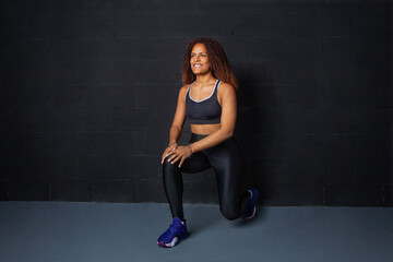 Chica afroamericana en ropa deportiva negra haciendo estocadas con pesas rojas, fondo negro. estilo...