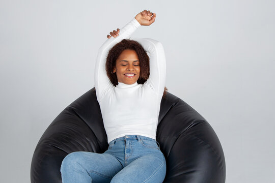 Chica afroamericana sentada en puf descansando y sonriendo. Mujer sonriendo