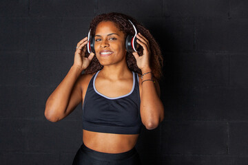 Chica afroamericana con ropa deportiva negra escuchando música con auriculares y sonriendo