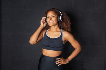 Chica afroamericana con ropa deportiva negra escuchando música con auriculares y sonriendo