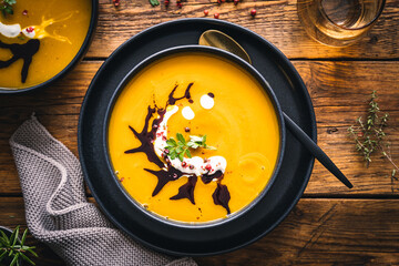 Frische Kürbissuppe in einem schwarzen Teller auf einem braunen rustikalen Tisch. Draufsicht, servierfertig, Herbst.