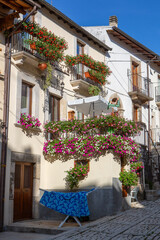 Mediterranean-style building with rustic stairs, flower-filled balconies, and laundry hanging under the sunny sky.