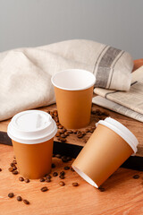 Disposable coffee cups placed on a wooden board with scattered coffee beans and a newspaper
