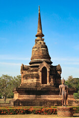 Fototapeta premium Standing buddha statue in front of a small pagoda next to the Wat Sa Si, Wat Sra Sri Temple at the Historical Park, the archaeological site, ancient ruins of Sukhothai, Thailand