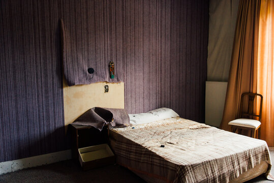 Chambre abandonn&eacute;e dans un hotel. Chambre d'hotel vandalis&eacute;e. Chambre squatt&eacute;e. Lit dans une vieille chambre sale. Mur violet et rideau orange. Chambre sale dans un hotel bas de gamme.