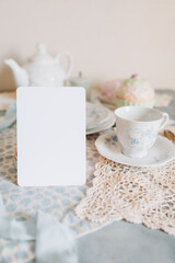 Mockup card,  teacup and saucer are on a table with a plate, tea time