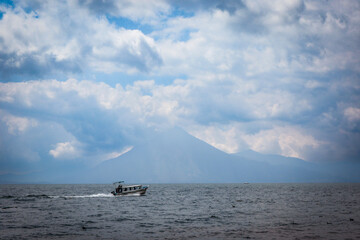 A boat gliding across Lake Atitlan in Guatemala under a cloudy sky with a backdrop of mountains