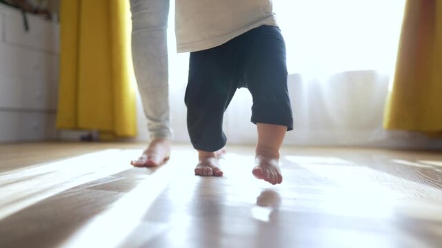 Mother and toddler together at home. Toddler learns to walk with mother support. Happy family moments. Toddler and mother enjoy bonding time. Learning to walk milestone. Toddler mother together.