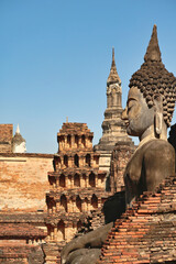A big buddha statue at the Wat Mahathat Temple with many chedis, stupas, towers in the background,...