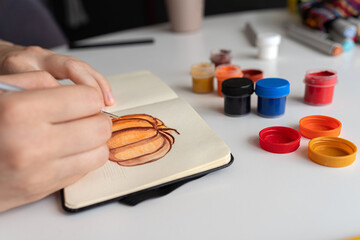 Finalizing a pumpkin painting with gouache in a sketchbook