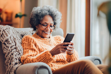 Senior woman embraces technology, smiling while using smartphone in cozy home environment. Tech-savvy grandmother with natural gray hair enjoys digital connection at home. 
