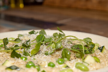 A delicious meal of courgette, broad bean and pea risotto, on a wooden kitchen table