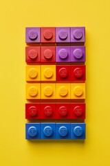Colorful toy blocks neatly stacked in a gradient from red to purple on a bright yellow background. --