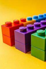 Obraz premium Colorful toy blocks neatly stacked in a gradient from red to purple on a bright yellow background. --