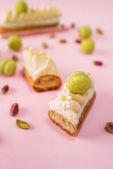 French sweet dessert Eclair cake cut in half with white creme and pistachio macarons on pink background