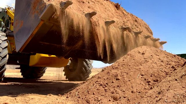 Front end loader dumping dry soil and resulting In lots of dust, sunny day