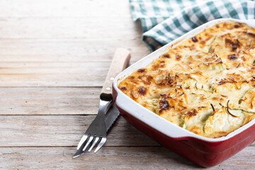 Casserole with cheese and gratin zucchini on wooden table. Copy space