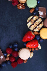 Macarons, chocolate, cookies, berries and various nuts on dark blue background. Top view.
