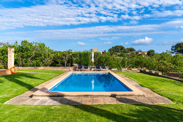 Schwimmbecken in einem Garten mit grüner Wieder und Palmen im Hintergrund im Sommerurlaub 