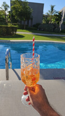 Aperol spritz cocktail in wine glass in front of pool and the garden.