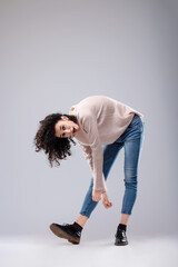 Young woman with curly hair bending over posing in studio