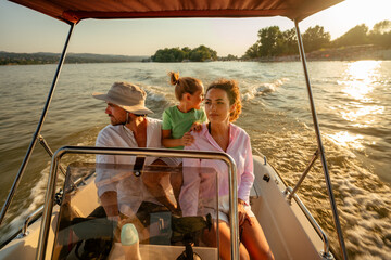A caucasian family of three enjoying a boat ride on a sunny day. The father is steering the boat,...