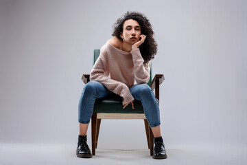 Young woman with hand on chin sitting on vintage armchair