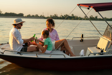 Happy family of three enjoying a boat ride on a calm lake during sunset. They are sitting on a...