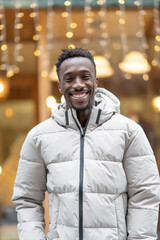 Fototapeta premium Man smiles warmly in a winter jacket, standing before glowing holiday lights.