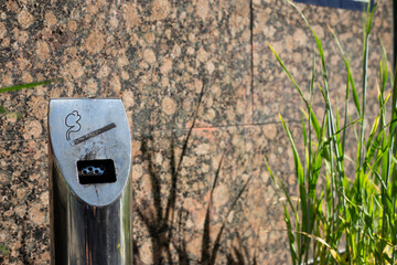 Modern ashtray on street in smoking area, metal pole with compartment for disposing of cigarettes,...