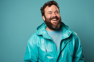 Fototapeta premium Portrait of a smiling man in his 40s wearing a vibrant raincoat isolated on pastel teal background