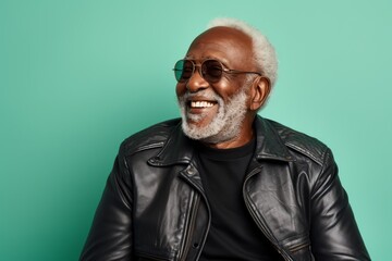 Fototapeta premium Portrait of a cheerful afro-american elderly man in his 90s sporting a classic leather jacket on pastel teal background