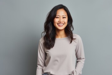 Obraz premium Portrait of a cheerful asian woman in her 20s sporting a long-sleeved thermal undershirt while standing against pastel gray background