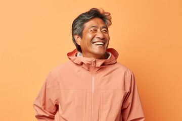 Fototapeta premium Portrait of a joyful asian man in his 60s wearing a functional windbreaker over pastel brown background