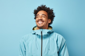 Obraz premium Portrait of a grinning afro-american man in his 30s wearing a lightweight packable anorak in front of soft blue background