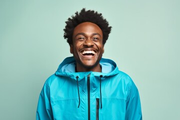 Fototapeta premium Portrait of a grinning afro-american man in his 30s wearing a lightweight packable anorak over soft blue background