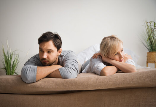Unhappy sad couple, bearded man, woman, husband and wife lay in bedroom bed, turned away from each other. Unlove crisis, sexual problem issues, relationship conflict, divorce people - concept image.