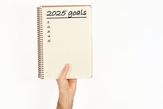 2025 goals written on a notebook held by a man. Isolated on white background.
